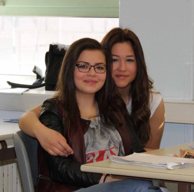 Zwei junge Frauen sitzen lächelnd an einem Schreibtisch.