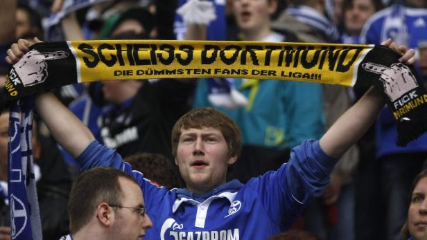Ein Schalke-Fan hält einen gelb-schwarzen Schal mit der Aufschrift „Scheiss Dortmund“ hoch.