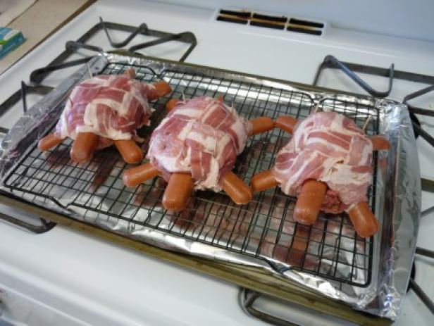 Drei Hotdog-Schildkröten, umwickelt mit Speck, liegen auf einem Backblech.
