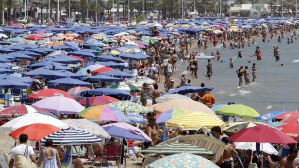 Ein überfüllter Strand mit vielen Menschen und bunten Sonnenschirmen.