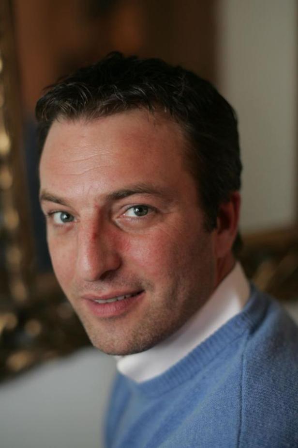 Ein Porträt eines Mannes mit dunklen Haaren und einem hellblauen Pullover.