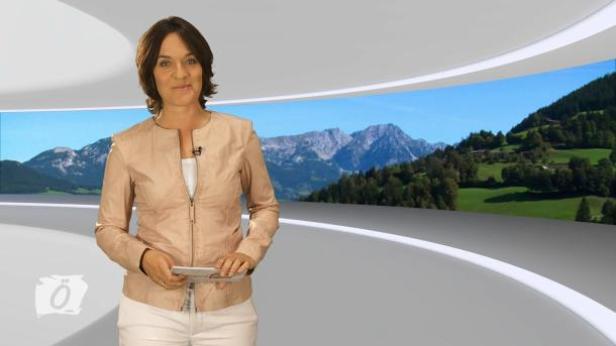 Eine Frau präsentiert vor einem Panorama mit Bergen und grünen Wiesen.