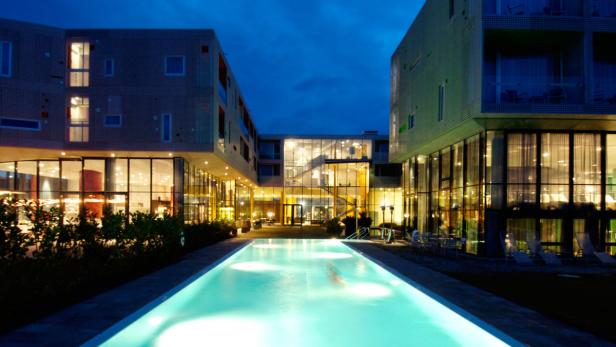 Ein beleuchteter Pool vor einem modernen Hotel bei Nacht.