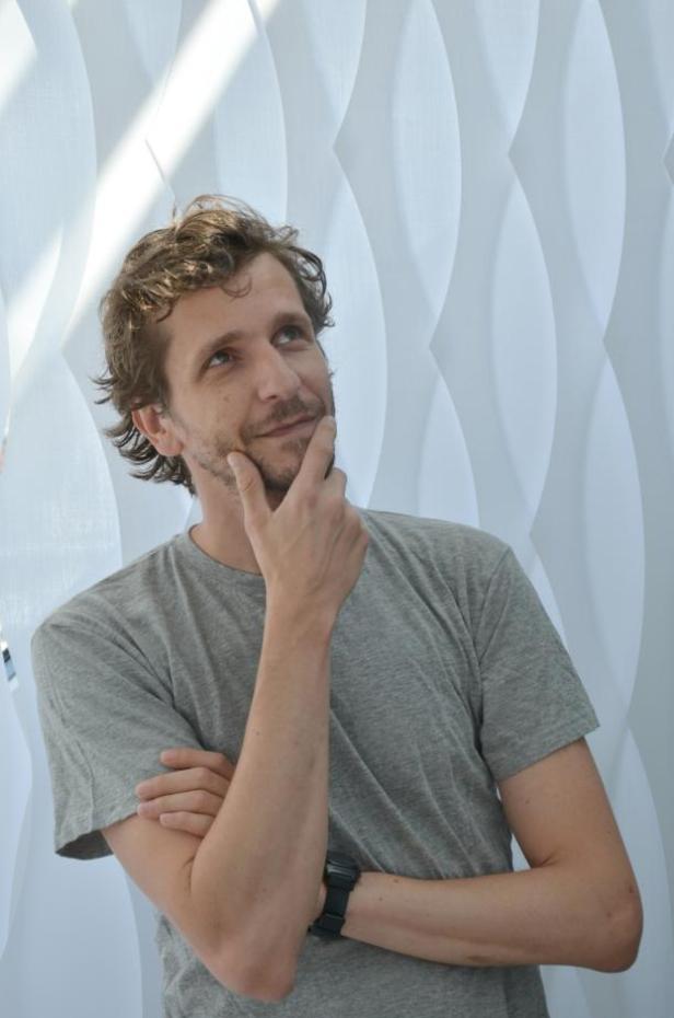 Ein Mann mit Bart und grauem T-Shirt denkt nach, den Finger am Kinn.