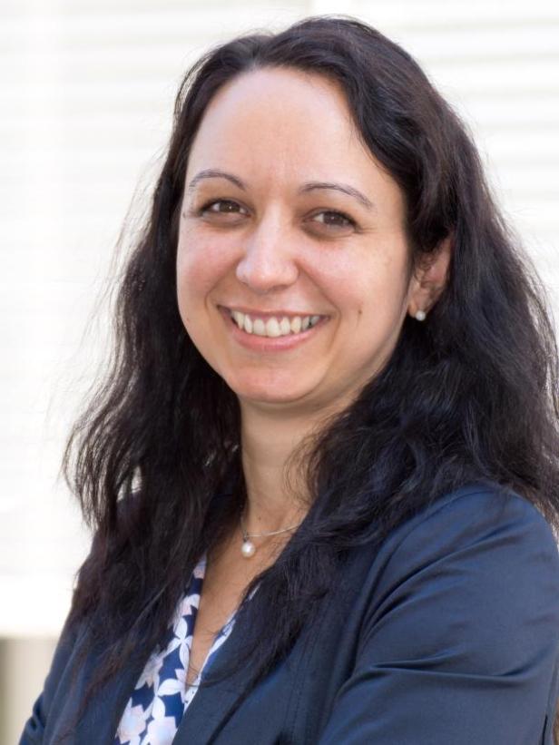 Eine lächelnde Frau mit dunklen Haaren und einem blauen Blazer.