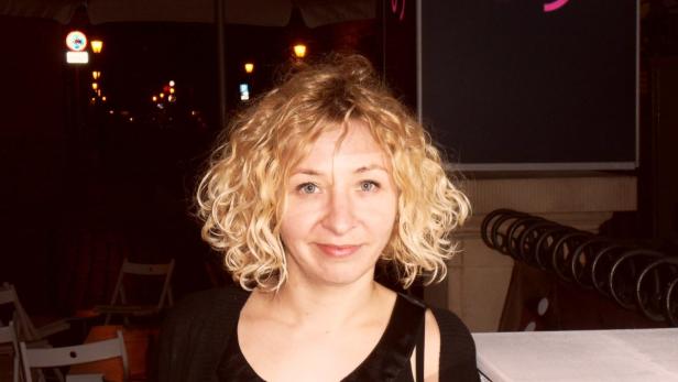 Eine Frau mit blonden Locken steht nachts vor einem Gebäude.