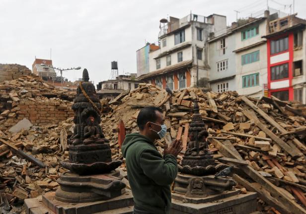 Ein Mann mit Maske betet vor Statuen inmitten von Trümmern in Nepal.