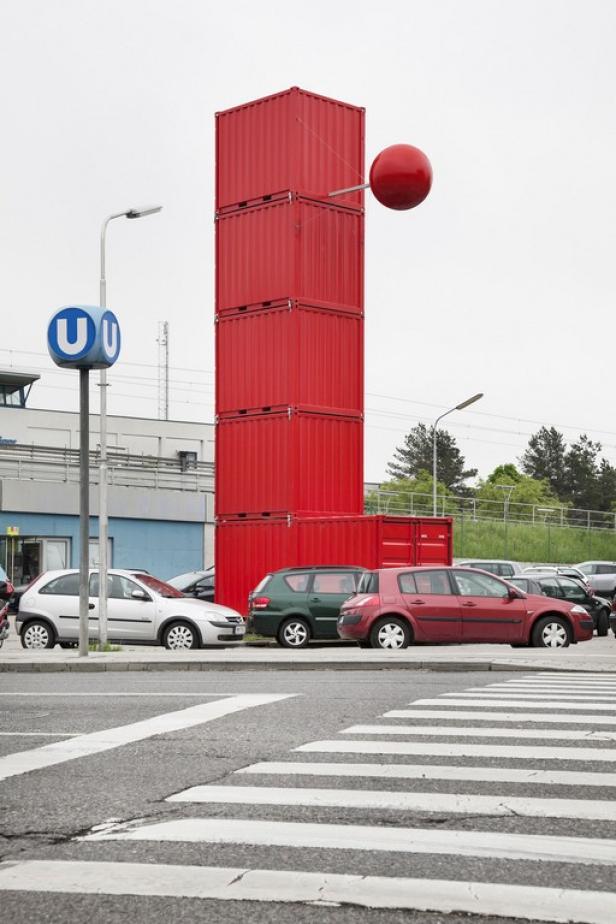 Ein Stapel roter Container mit einer roten Kugel davor, neben einem U-Bahn-Schild.