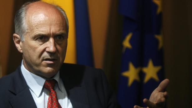 Ein Mann im Anzug gestikuliert vor Flaggen.