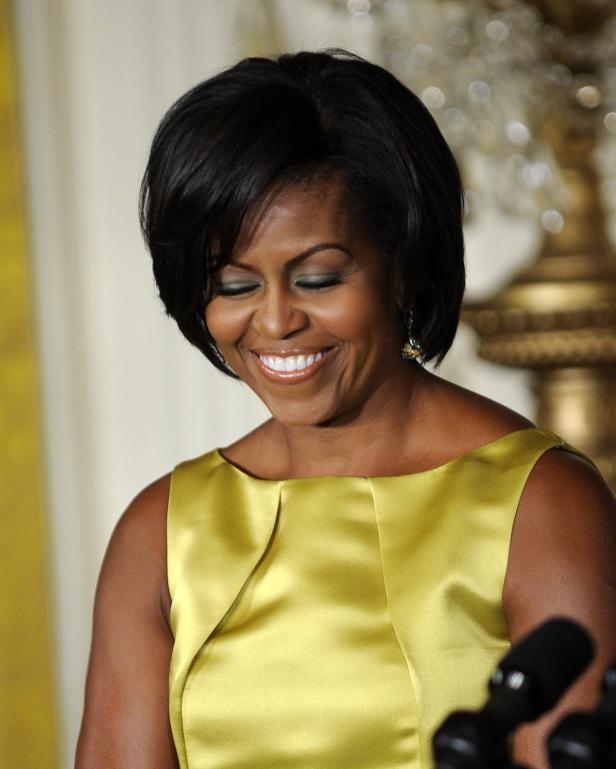 Michelle Obama lächelt in einem gelben Kleid.