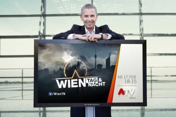 Ein Mann lächelt hinter einem Bildschirm, der die Sendung „Wien Tag & Nacht“ auf ATV ankündigt.