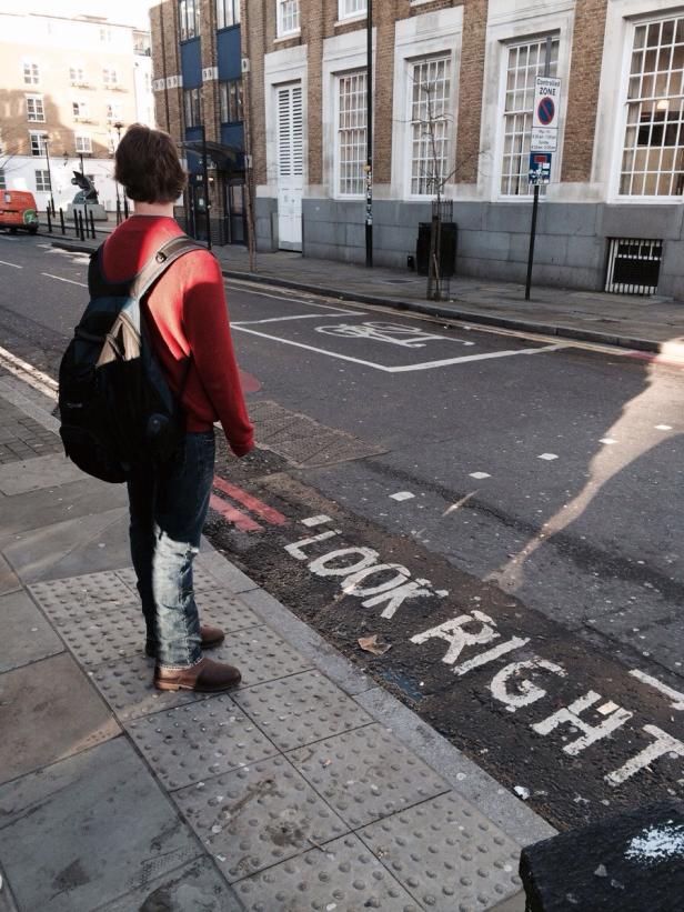 Ein Mann mit Rucksack steht an einer Straße mit der Aufschrift „Look Right“.