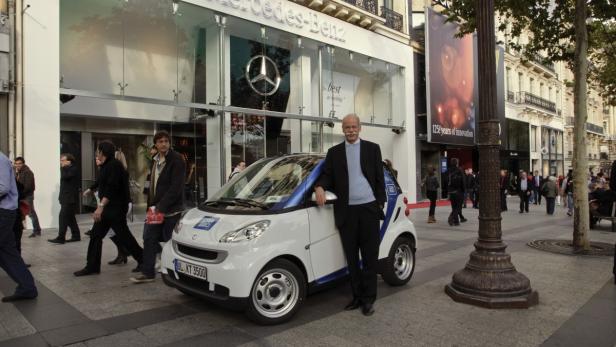 Dieter Zetsche posiert vor einem Smart vor einem Mercedes-Benz Geschäft.