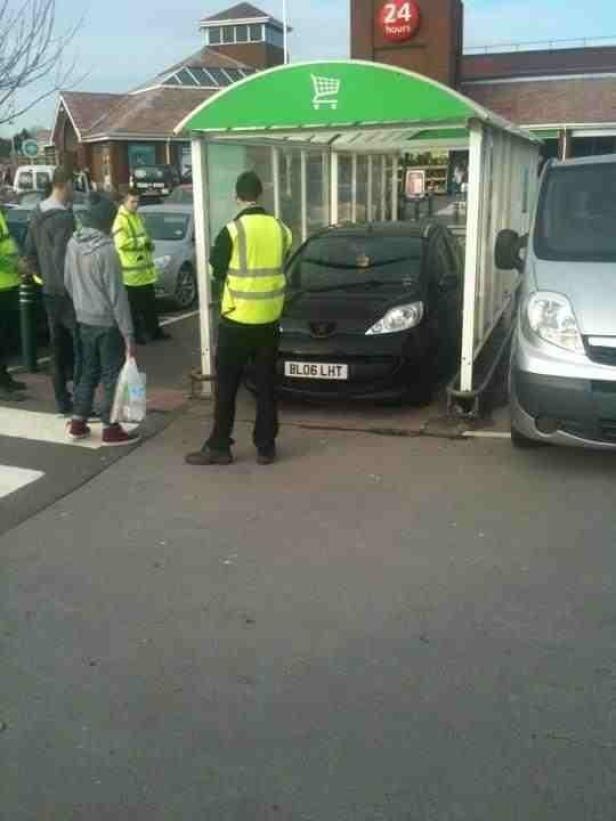 Ein schwarzer Kleinwagen ist in einen Einkaufswagen-Unterstand vor einem Supermarkt gefahren.