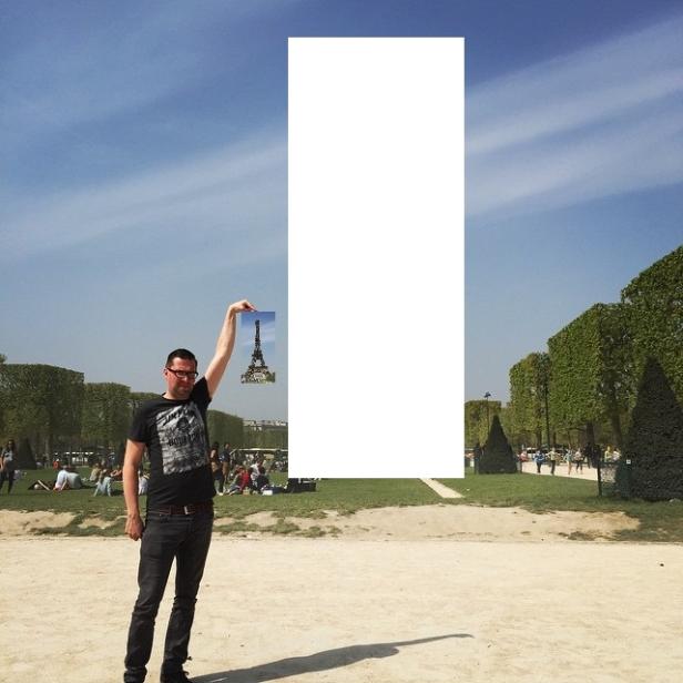 Ein Mann hält ein Bild des Eiffelturms in die Höhe, wobei ein weißes Rechteck einen Teil des Turms verdeckt.