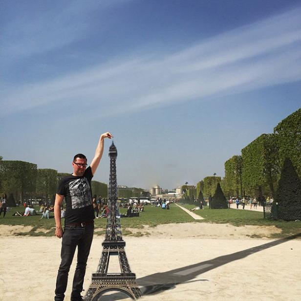 Ein Mann posiert mit einem Modell des Eiffelturms im Park.