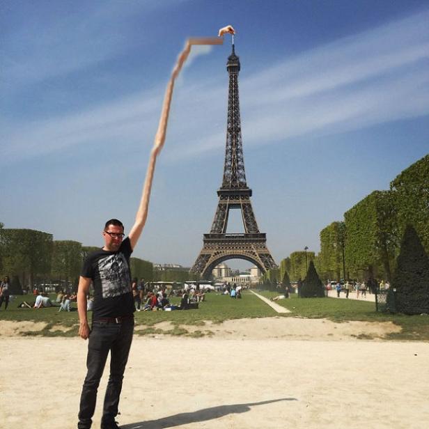 Ein Mann mit einem extrem langen Arm „berührt“ die Spitze des Eiffelturms in Paris.