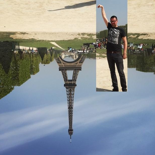 Ein Mann scheint den Eiffelturm mit seiner Hand zu berühren; die Aufnahme ist auf dem Kopf stehend.