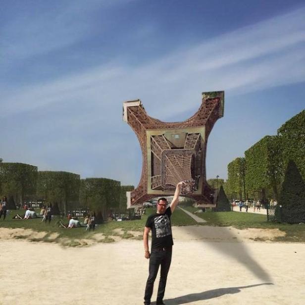 Ein Mann hält im Park eine optische Täuschung der Spitze des Eiffelturms hoch.