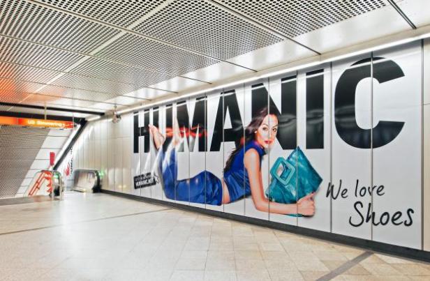 In einer U-Bahn-Station wirbt ein großes Plakat für „Humanic“-Schuhe mit einer darauf liegenden Frau.