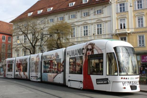 Straßenbahn - Graz Eine Straßenbahn mit Werbung für HUMANIC fährt durch eine Stadt.
