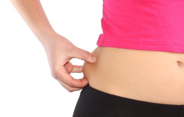 Eine Frau zwickt ihre Haut am Bauch.