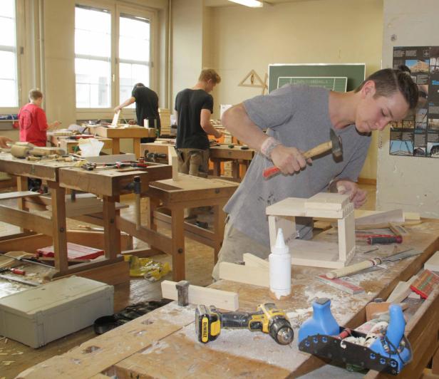 In einer Werkstatt hämmert ein Jugendlicher ein Holzstück zusammen.