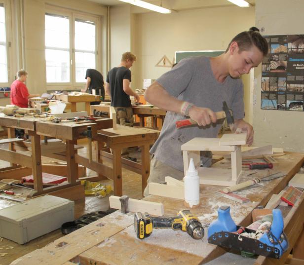 Ein junger Mann hämmert in einer Werkstatt ein Holzstück zusammen.