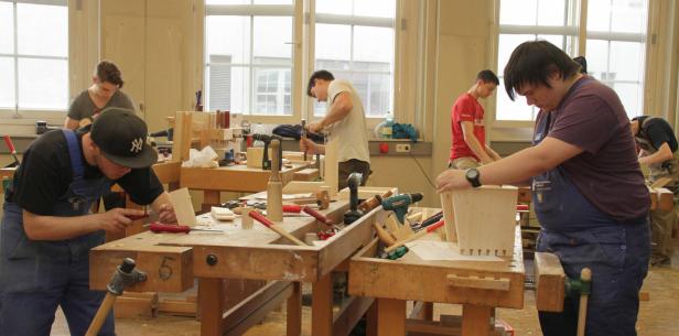 Mehrere Personen arbeiten in einer Werkstatt an Holzarbeiten.