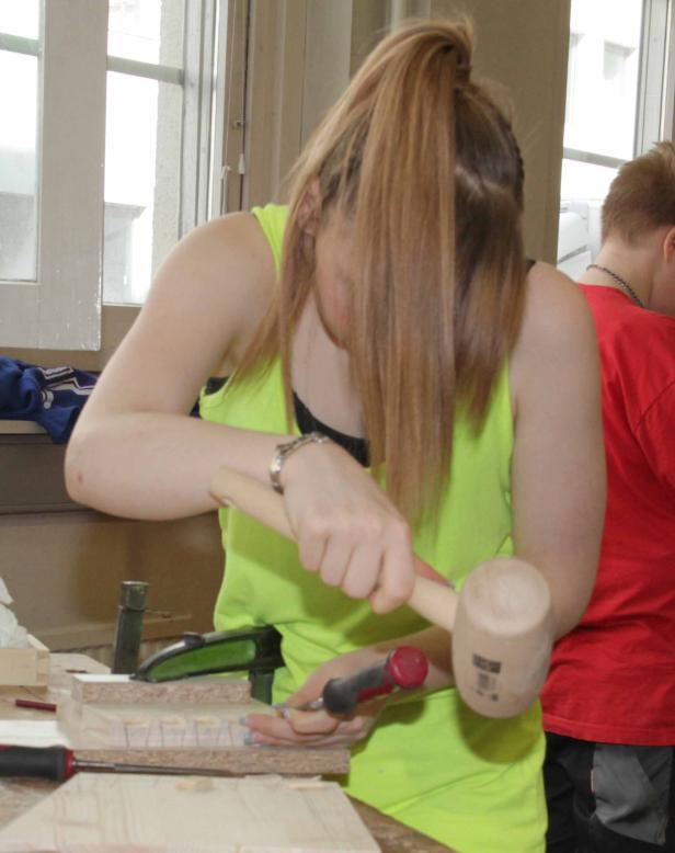 Eine Frau arbeitet mit einem Stecheisen und einem Holzhammer an einem Werkstück.