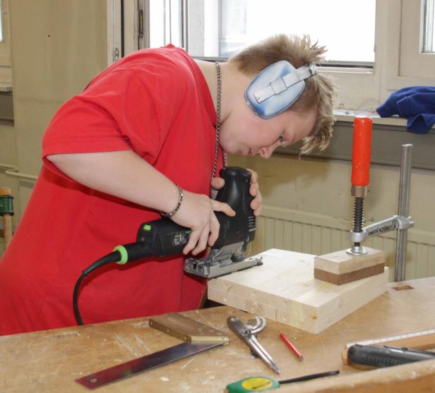 Eine Person mit Gehörschutz sägt ein Holzbrett mit einer Stichsäge.