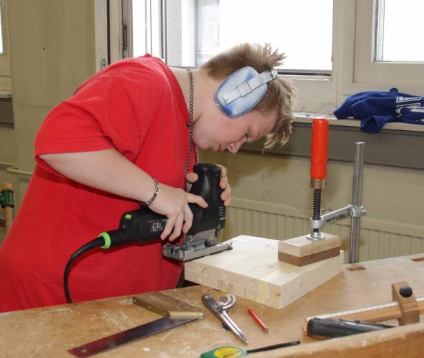 Eine Person mit Gehörschutz sägt ein Holzbrett mit einer Stichsäge.
