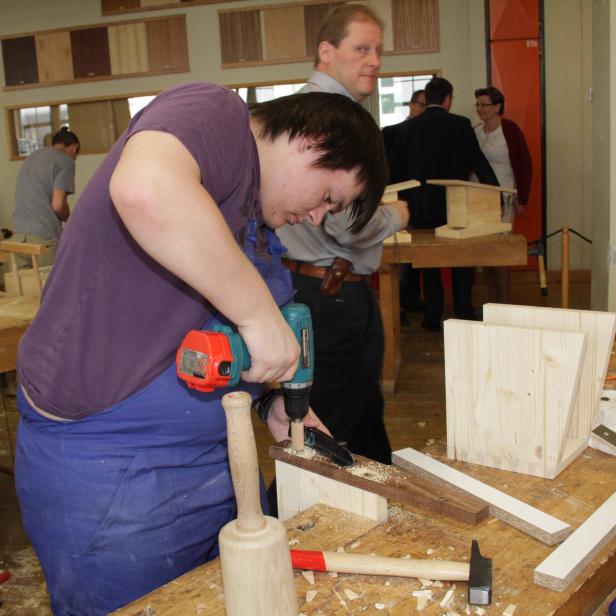 Ein Mann bohrt in einer Werkstatt ein Loch in ein Holzstück.