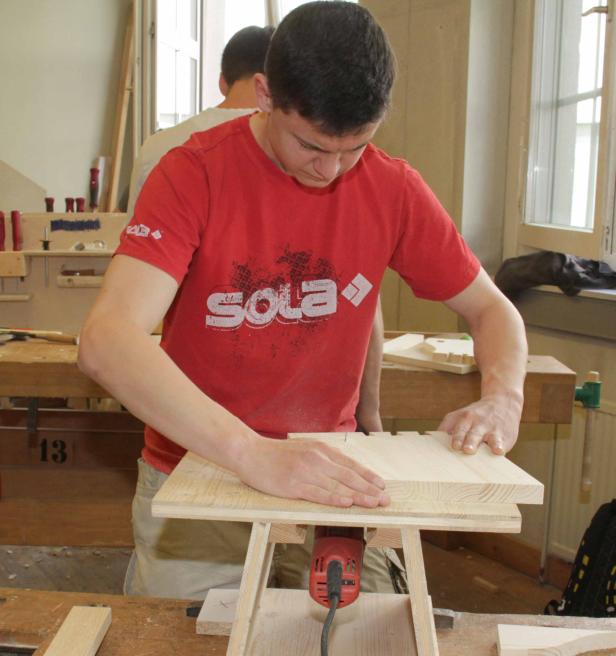 Ein junger Mann arbeitet in einer Werkstatt an einem Holzstück.