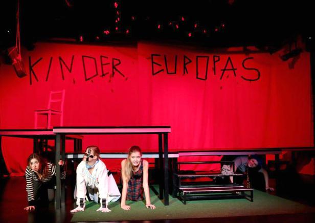 Eine Theaterszene mit dem Titel „Kinder Europas“ im roten Bühnenlicht.