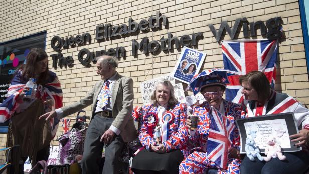 Eine Gruppe Menschen feiert vor dem „Queen Elizabeth The Queen Mother Wing“ Gebäude mit Union-Jack-Dekorationen.