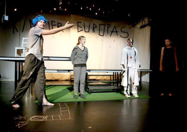 Eine Theaterszene mit vier Schauspielern vor einer Wand mit der Aufschrift „Kinder Europas“.