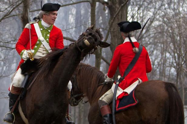 Zwei Männer in historischen Uniformen reiten auf Pferden, wobei eines der Pferde die Zähne zeigt.