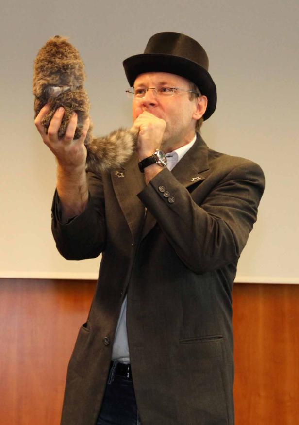 Ein Mann mit Hut bläst in ein ungewöhnliches, fellartiges Instrument.