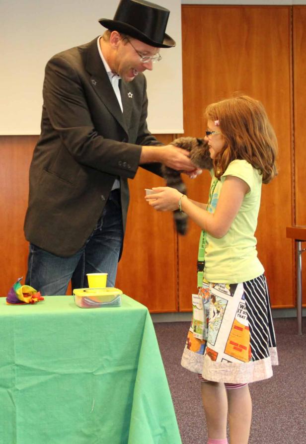 Ein Zauberer mit Zylinder präsentiert einem Mädchen einen Waschbären.