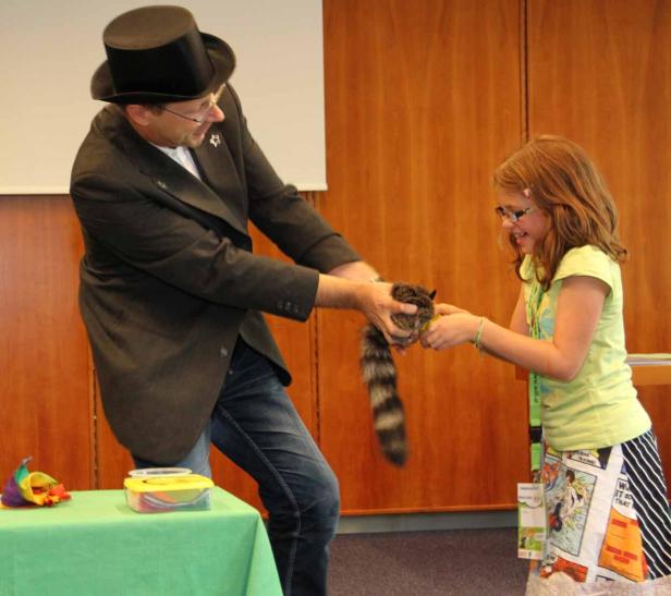 Ein Zauberer übergibt einem Mädchen einen Waschbären.
