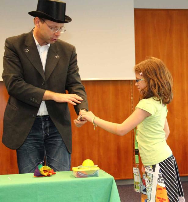 Ein Zauberer führt einem Mädchen einen Trick mit einem Löffel vor.