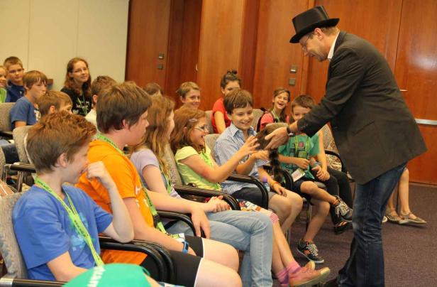 Ein Zauberer führt vor einer Gruppe von Kindern einen Trick mit einem Waschbären vor.