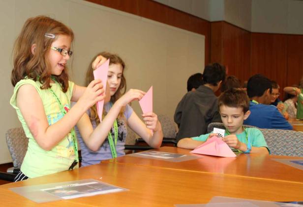 Kinder sitzen an einem Tisch und falten Papierfiguren.