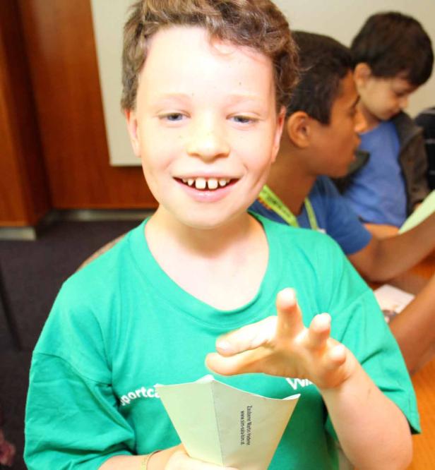 Ein lächelnder Junge mit grünem T-Shirt hält einen Papierhut in der Hand.