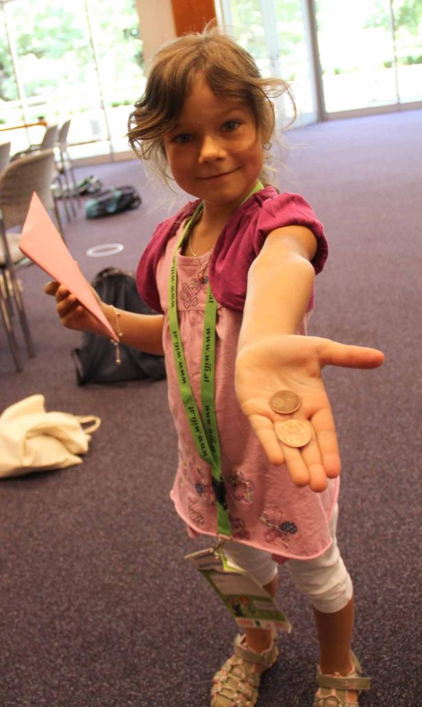 Ein junges Mädchen zeigt zwei Münzen in ihrer Hand.