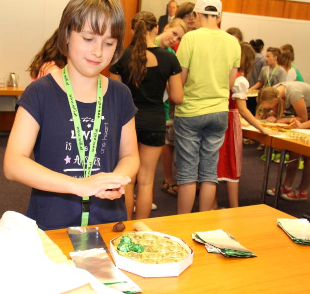 Ein Mädchen formt Pralinen auf einem Tisch, an dem weitere Kinder arbeiten.