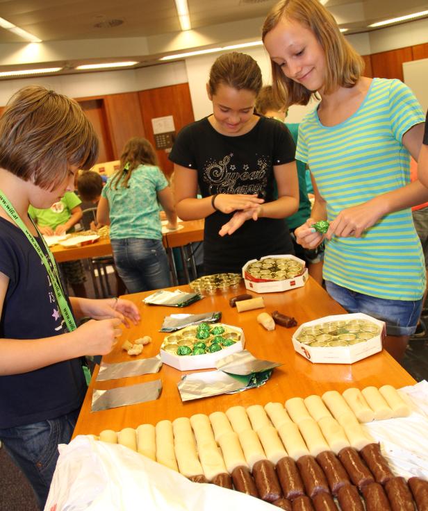 Kinder verpacken Marzipankartoffeln an einem Tisch.