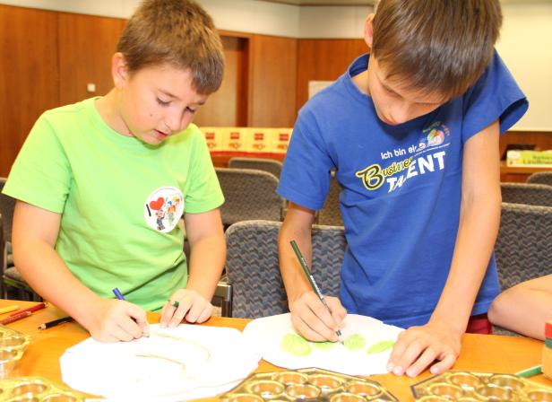 Zwei Jungen sitzen an einem Tisch und malen mit Buntstiften auf Papier.