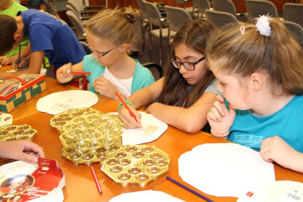 Kinder basteln mit Pinsel und Farbe an Tischen mit Pralinenformen.